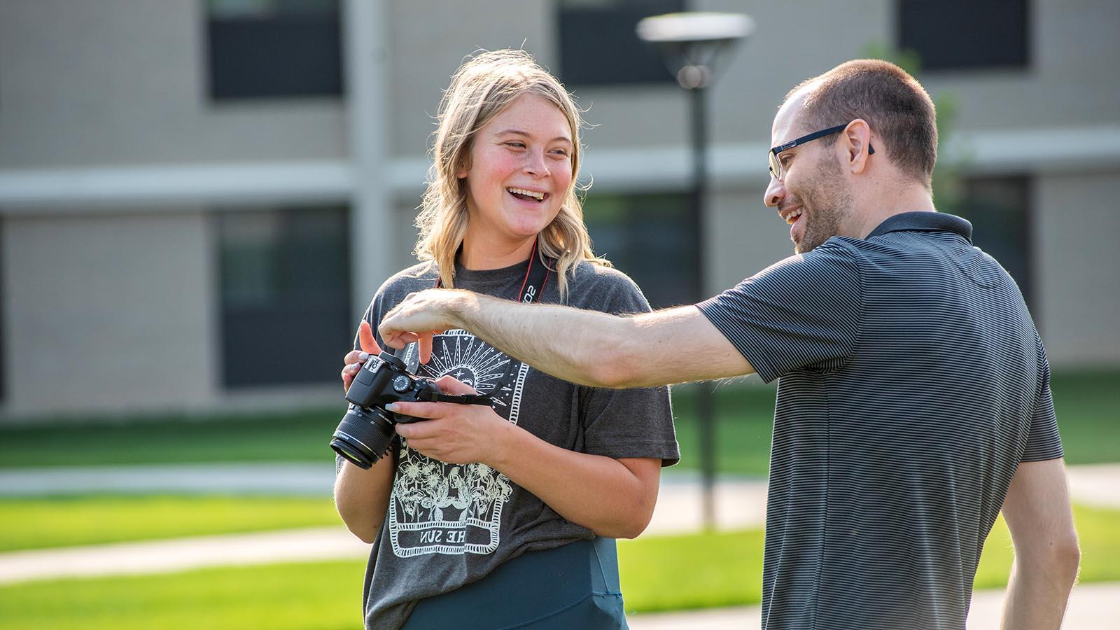 Photography professor smiling and pointing to controls on year-round campus student’s camera
